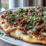 Knuspriges Türkisches Lahmacun mit Lamm, frischen Kräutern, appetitlich serviert.