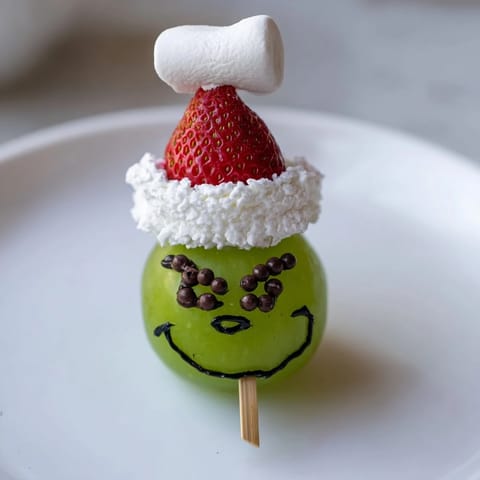 Bright green Grinch face snack made with grapes, waiting for a holiday movie night treat.