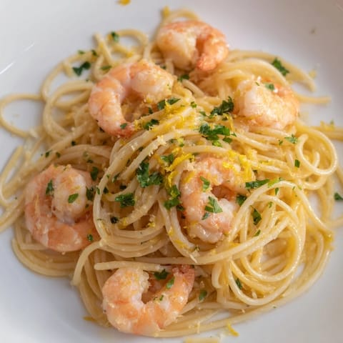 Teller mit dampfender Lemon Garlic Shrimp Pasta, bestreut mit frischen Kräutern und serviert mit einer Scheibe Zitrone für frischen Abschluss.