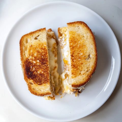 Ein würziger Drei-Käse-Grilled Cheese mit goldbrauner Kruste, servierfertig mit Tomatensuppe zum Tunken.