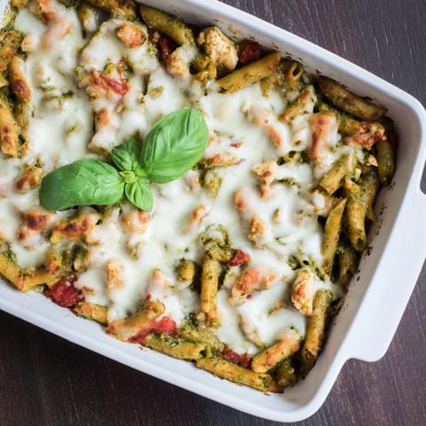 Goldenes Pesto Chicken Pasta Bake mit geschmolzenem Mozzarella und frischen Basilikumblättern garniert.