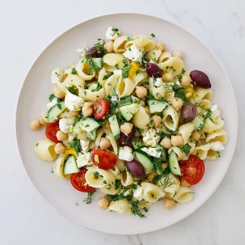 Frische Lemon Herb Chickpea Pasta Salad mit gewürfelten Gurken und Kirschtomaten, cremigem Feta und Kräutern auf dem Teller.