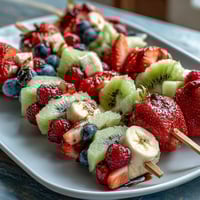 Frische rote Erdbeeren, weiße Bananen und blaue Heidelbeeren auf Stäbchen für ein festliches Dessert.